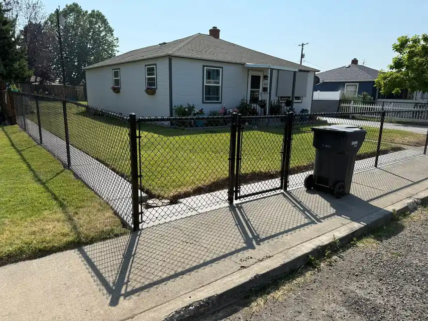Black vinyl-coated chain-link fence and walk gate around the front yard of a small white house