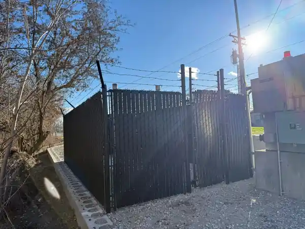 A black-slat chain-link utility enclosure with barbed wire along the top