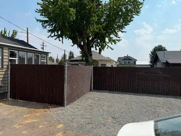Brown Viewguard privacy chain link enclosing a gravel back lot beside a house