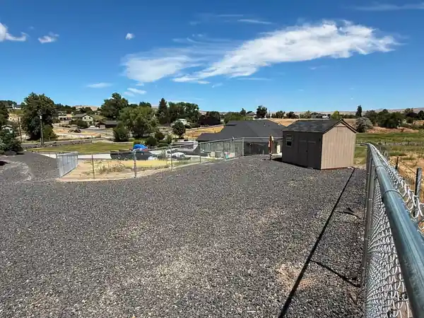 The top rail of a new galvanized 5 foot chain-link fence running toward a rural house in Selah