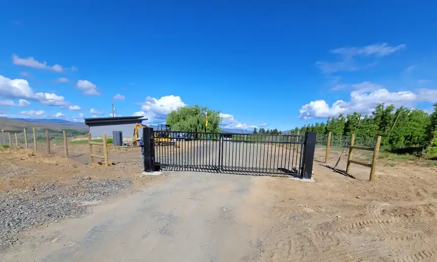 A black rolling gate hung between new posts along an orchard road