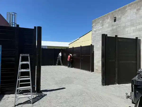 L S Fencing crew mounting tall dark steel privacy panels beside a block building
