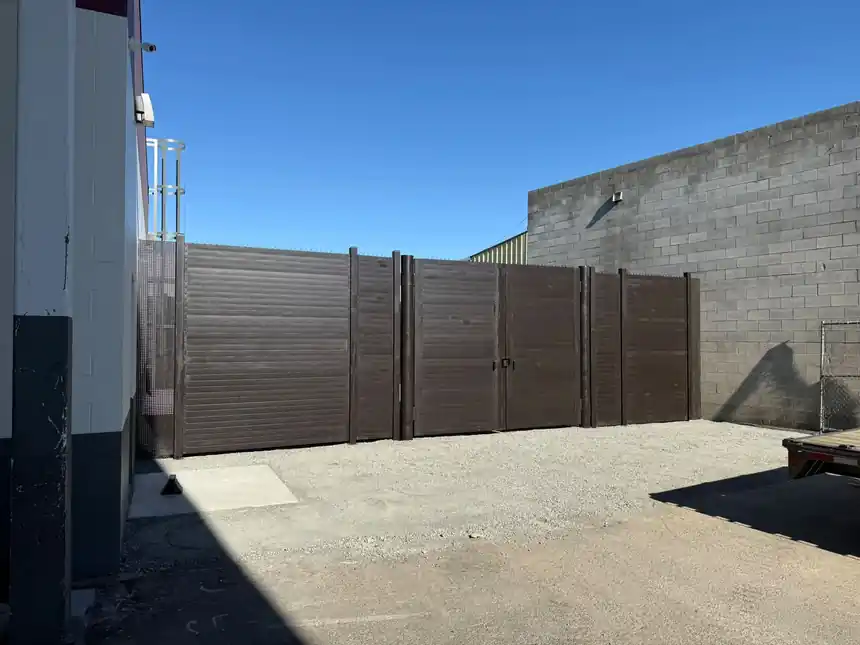 A finished 10 foot dark steel privacy fence with double gates against a block wall