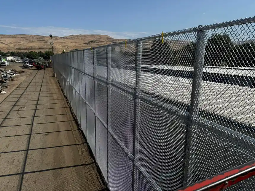 Looking along the top rail of a tall commercial chain-link wall, line posts marching away at an even spacing