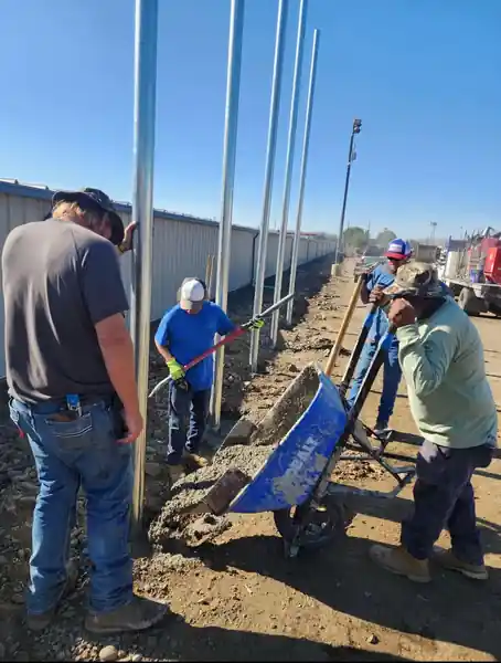 L S Fencing crew setting tall line posts on a job site, a wheelbarrow beside the hole