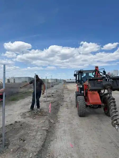 An L S Fencing crew member at a fence post beside the auger tractor